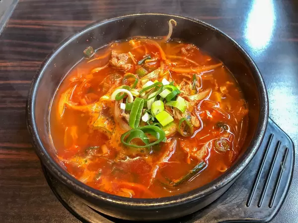 Würziger Eintopf mit Rindfleisch, Reis und Gemüse in schwarzem Topf auf Holztisch