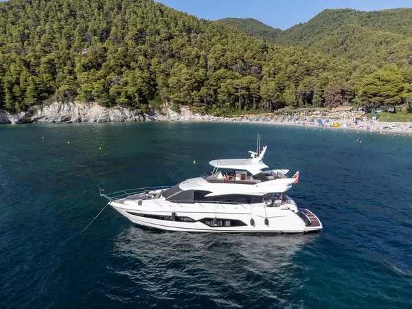 Yacht off the coast of Skopelos in front of the crowded Kastani beach surrounded by wooded hills