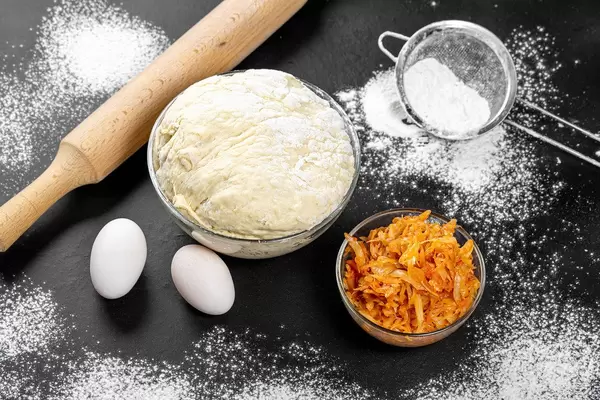 Yeast dough and fried cabbage on the table with flour and eggs