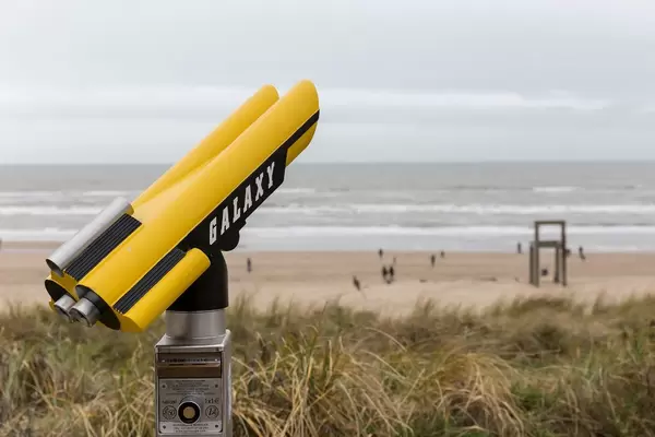 Yellow-black binoculars with inscription Galaxy in front of the beach of Zandvoort with giant chair