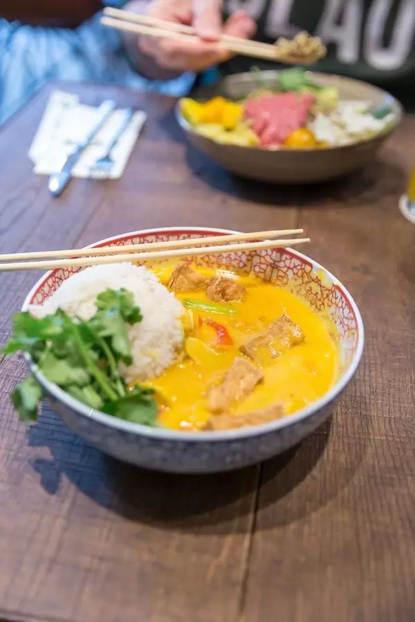 Yellow coconut tofu curry as vegan Asian lunch with Jasmin fragrant rice and baby spinach, in a traditional bowl with chopsticks, on a wooden table