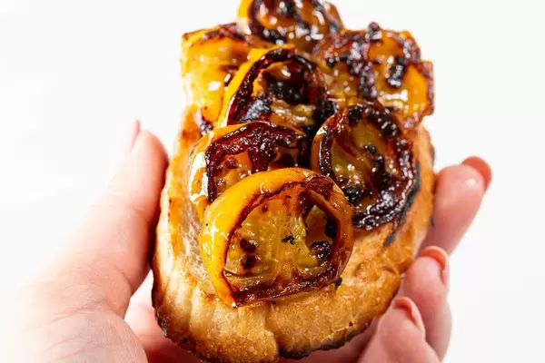 Yellow grilled tomatoes on toasted bread in a woman's hand
