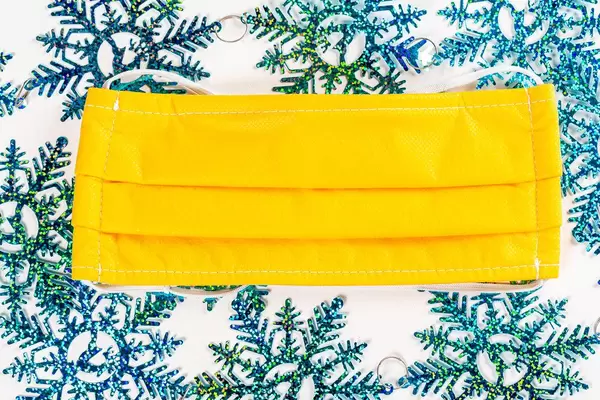 Yellow medical mask on blue snowflakes background