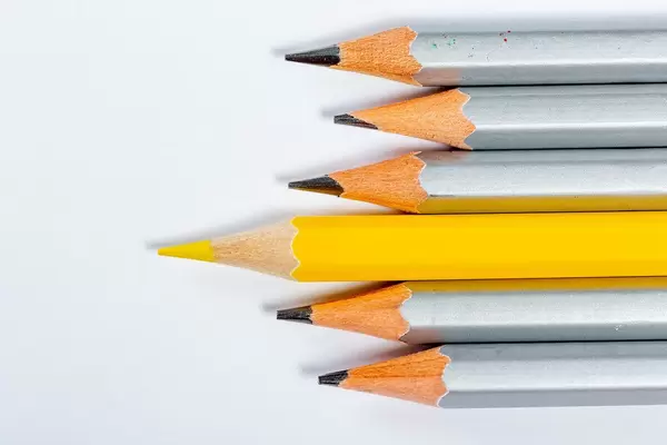 Yellow pencil standing out from crowd of plenty identical grey fellows on white background