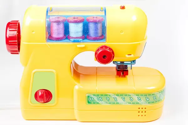 Yellow plastic sewing machine-toy for children on a white background (Flip 2020)
