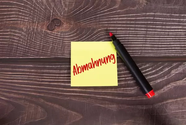 Yellow sticky note with Abmahnung text on wooden table