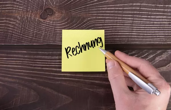 Yellow sticky note with Rechnung text on wooden table