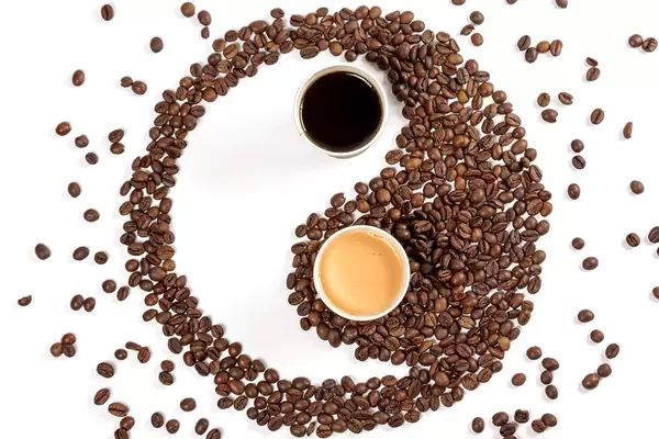 Yin yang symbol made from roasted coffee beans, espresso and coffee with milk in paper cups