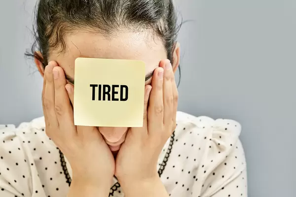 Young businesswoman and a sticker on her head with 'tired' note