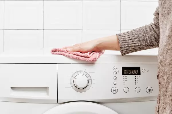 Young female cleans the plastic surface of a modern washing machine
