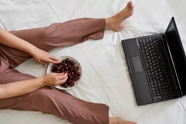 Young female eating fresh cherry fruits and watching movie on the laptop