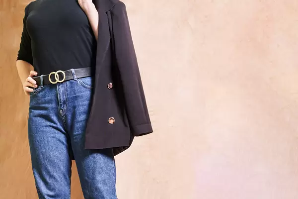 Young female in jeans holding black suit jacket on her shoulder