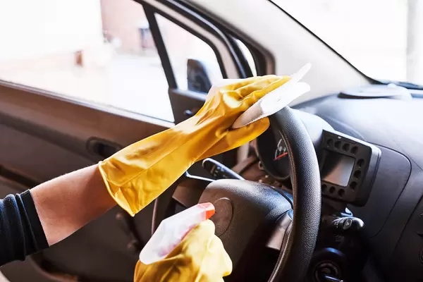 Young female sanitizing car interior for covid prevention