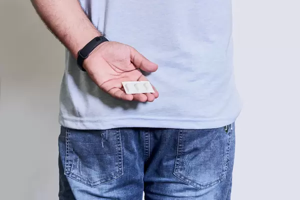 Young male suffering from hemorrhoids holds hemorrhoidal suppositories in hands