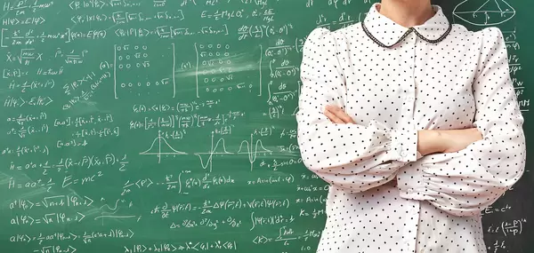 Young scientist standing over chalkboard filled with different scientific formulas