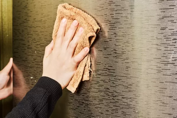Young woman cleaning a fridge surface in a kitchen with a microfiber cloth