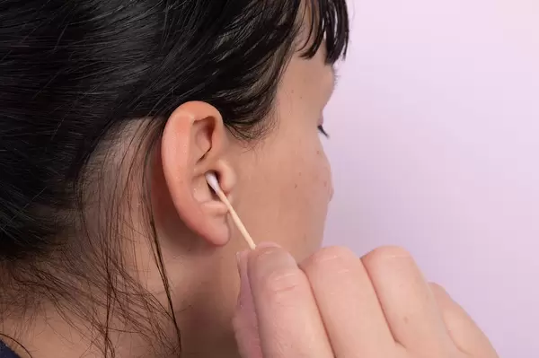 Young woman cleaning her ears with cotton sticks on pink background
