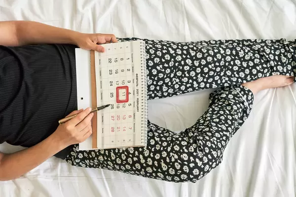 Young woman holding calendar with marked day of beginning of menstrual cycle days