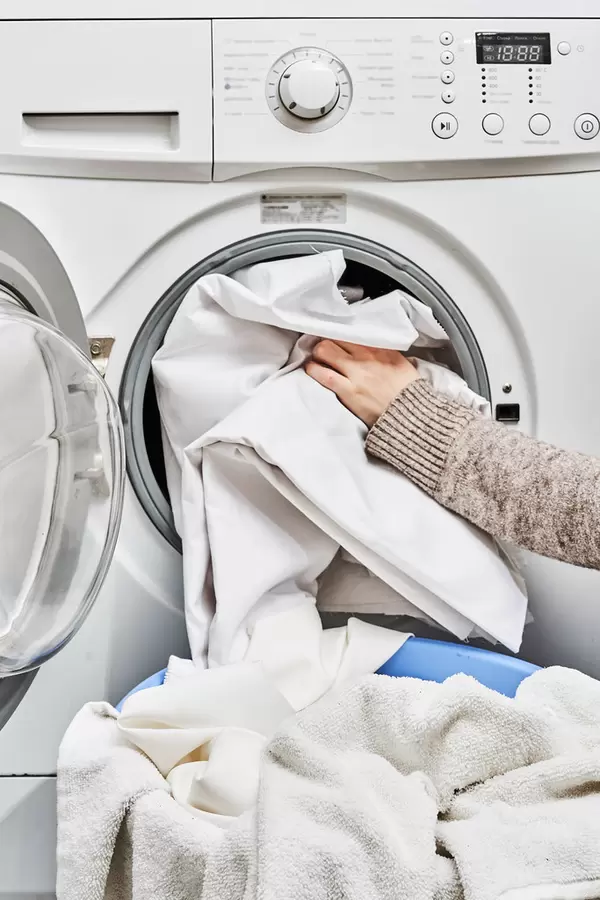 Young woman loads wash machine for cleaning laundrys