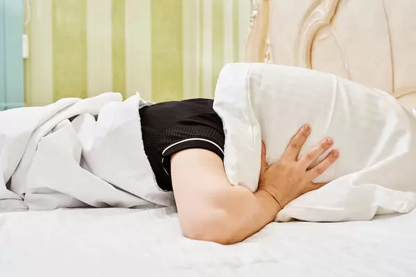 Young woman lying in bed suffering from sound covering head and ears with pillow