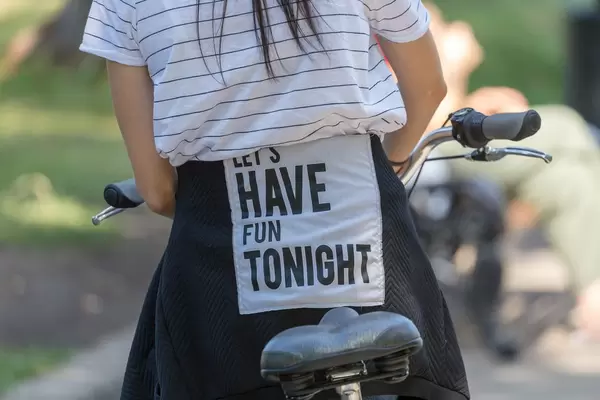 Young woman on bicycle with "let's have fun tonight" written on her back