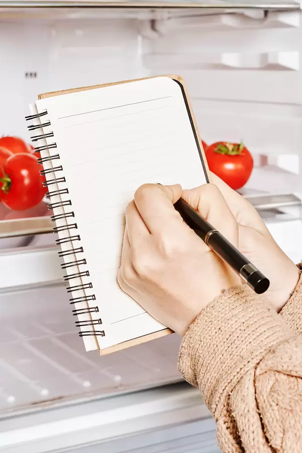 Young woman writing shopping list near the open refrigerator