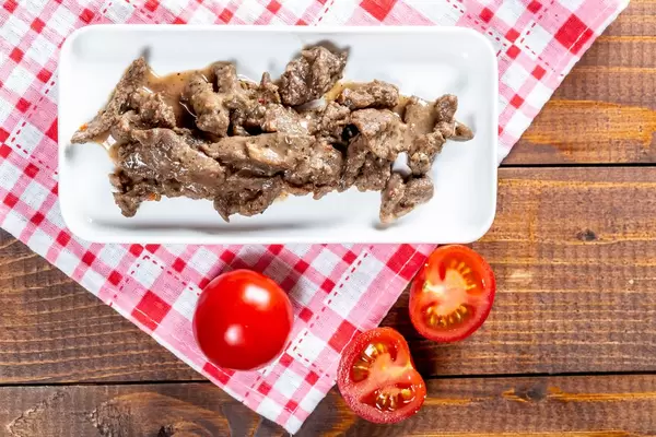 Zartes saftiges Rindsragout auf weißer Platte mit Tomaten auf Holztisch