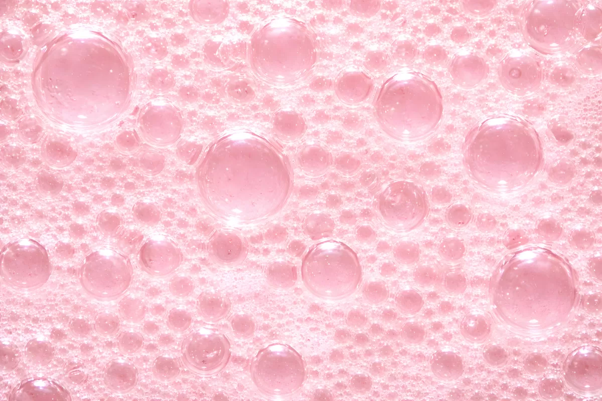 Zartrosa Seifenblasen auf schaumiger Wasseroberfläche