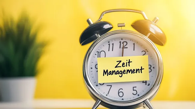 Zeitmanagement: Wecker mit Notizzettel auf gelbem Hintergrund