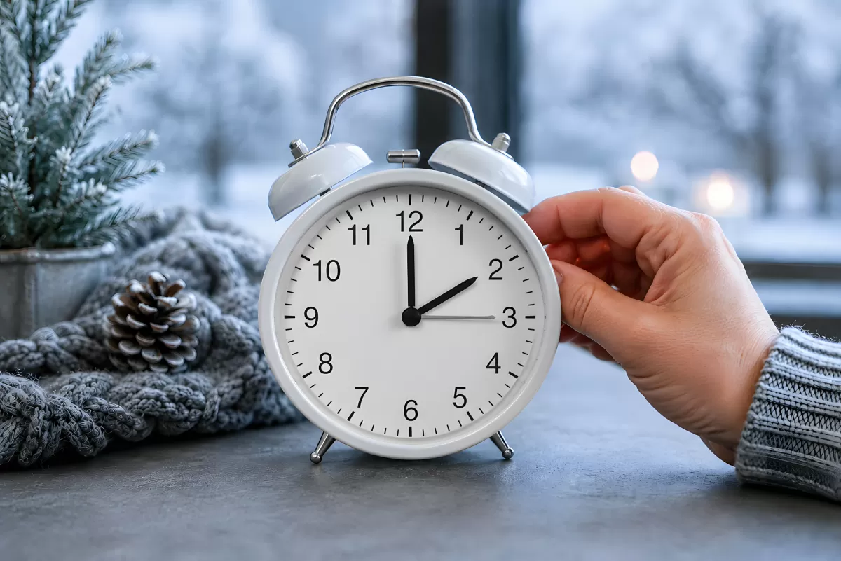 Zeitumstellung: Hand stellt weißen Wecker auf Winterzeit um