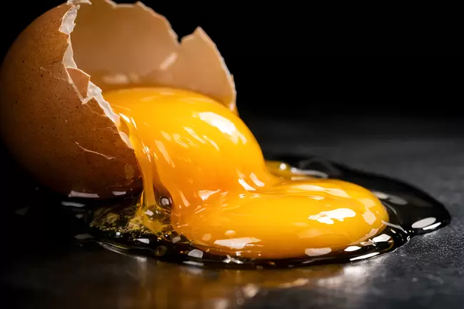 Zerbrochenes Ei: Gelber Dotter fließt auf schwarzem Hintergrund