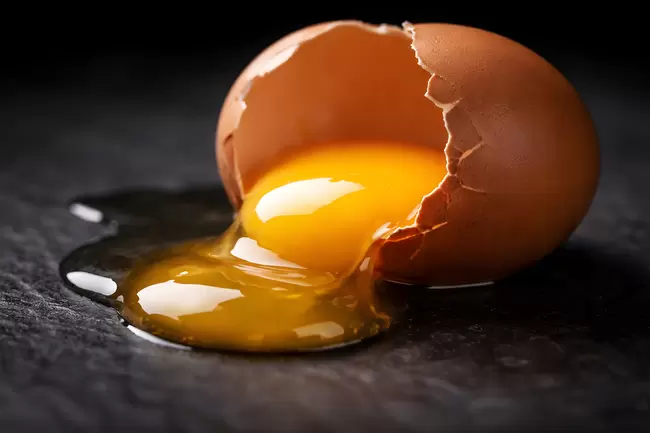 Zerbrochenes Ei mit gelbem Dotter auf dunkler Fläche