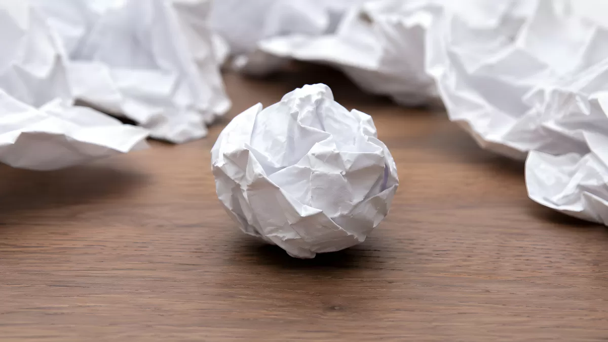 Zerknüllte Papierkugel auf Holztisch zwischen Papierknäueln
