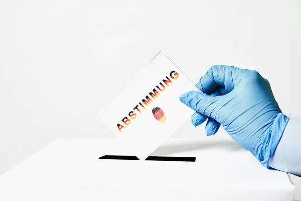 Zettel mit Schrift "Abstimmung" und Fingerabdruck in den Farben der deutschen Flagge in der Hand eines Wählers