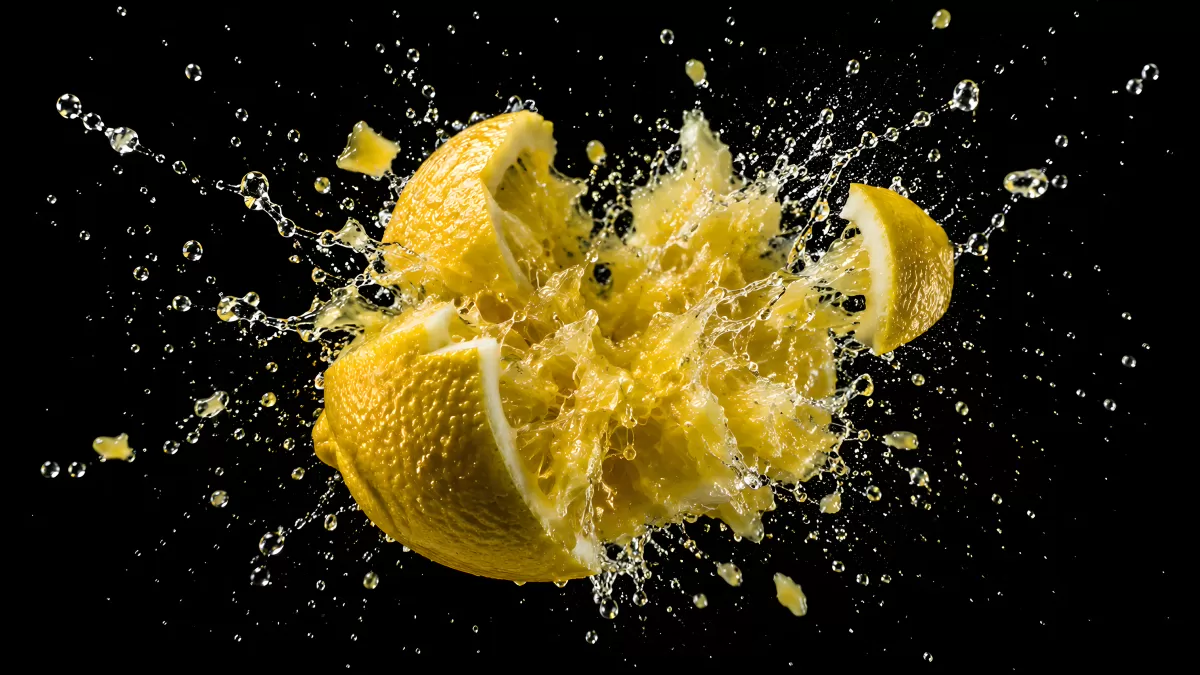 Zitrone explodiert mit Saft-Spritzern vor schwarzem Hintergrund