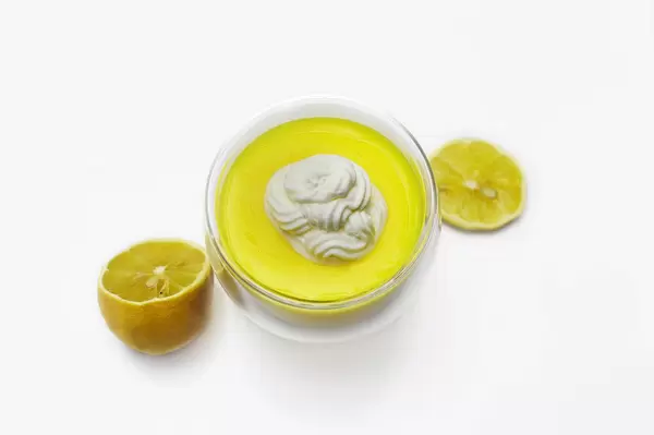 Zitronencreme mit Schlagsahne in Glasschale, daneben aufgeschnittene Zitrone vor weißem Hintergrund