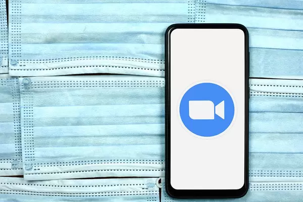 Zoom app logo on smartphone screen over the face masks. Global company during coronavirus crisis