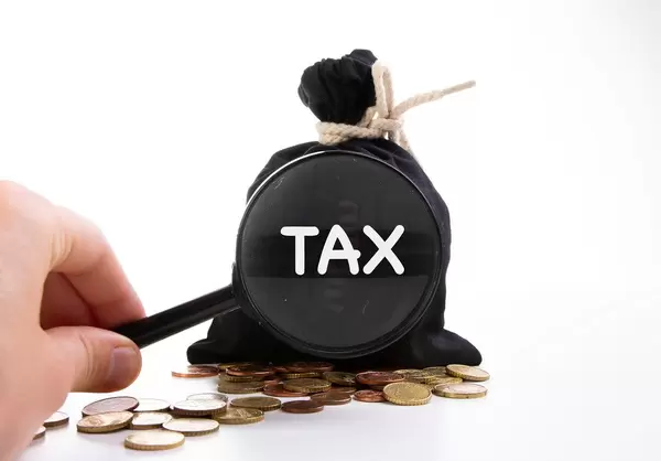 Zugeknoteter Geldsack hinter Kleingeld und der Aufschrift Steuern, vergrößert dargestellt und einer Lupe