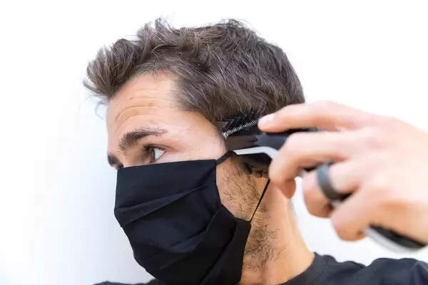 Zuhause wie beim Friseursalon mit dem Philips QC5115/15 Haarschneider. Mann schneidet sich die Haare selber mit Mundschutz. Porträt vor weißem Hintergrund