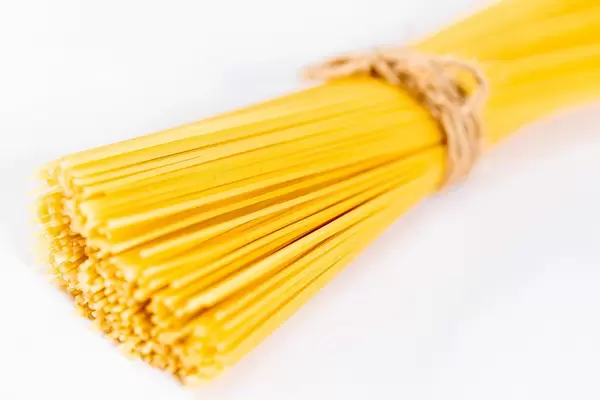 Zusammengebundene, goldgelbe Spaghetti vor weißem Hintergrund