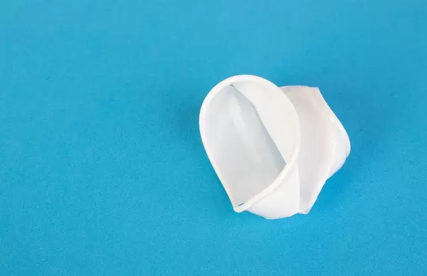 Zusammengeknüllter Einweg-Plastikbecher vor blauem Hintergrund repräsentiert das Müllproblem