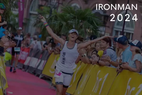Zuschauer beim Anfeuern der Sportlerin, während der letzten Meter des Marathons beim Dreikampf, neben dem Bildtitel "Ironman 2024"