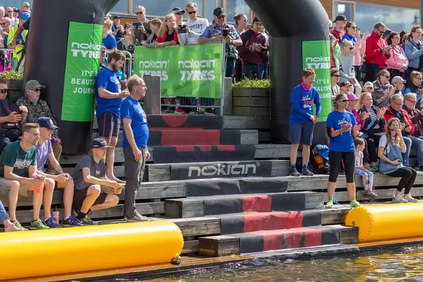 Zuschauer sitzen auf einem Holzpodest am Ufer des Sees Vesijärvi in Lahti, um die Triathlon-Sportler bei der Ironmandisziplin Schwimmen anzufeuern