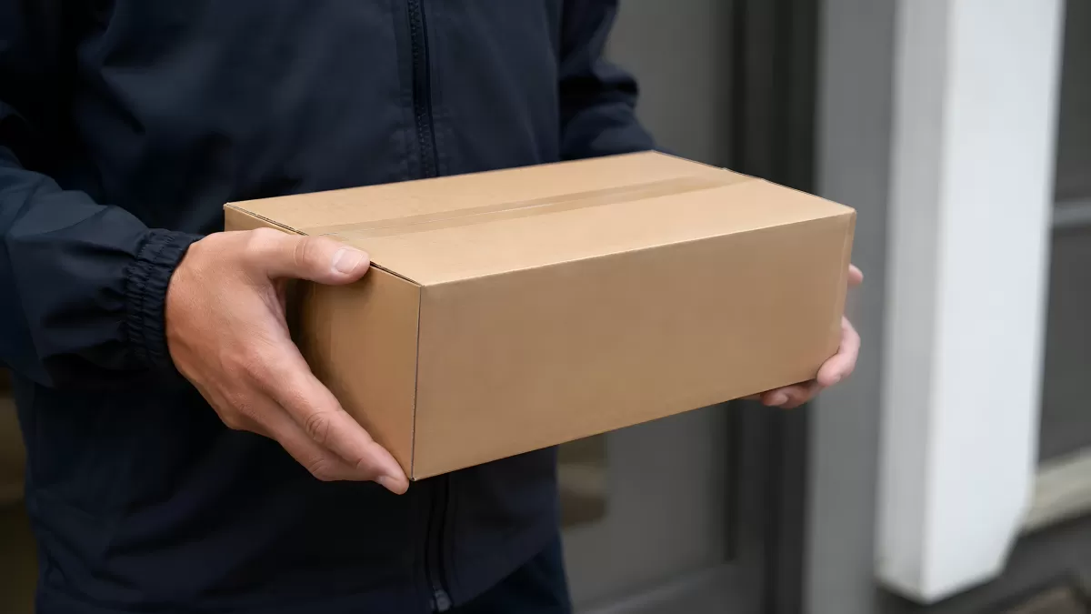 Zusteller hält Paket aus Karton vor Haustür