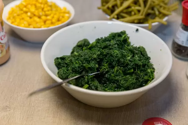 Zutaten für Raclette wie Spinat, Maissalat, ganze Bohnen, Pfeffermühle und Soße auf Holztisch