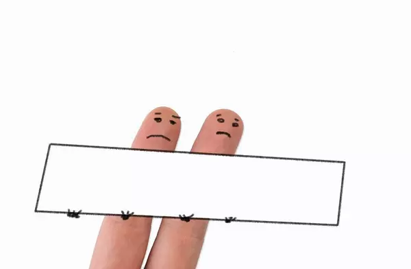 Zwei angemalte Finger mit unglücklichem Gesicht halten ein leeres Schild in den Händen