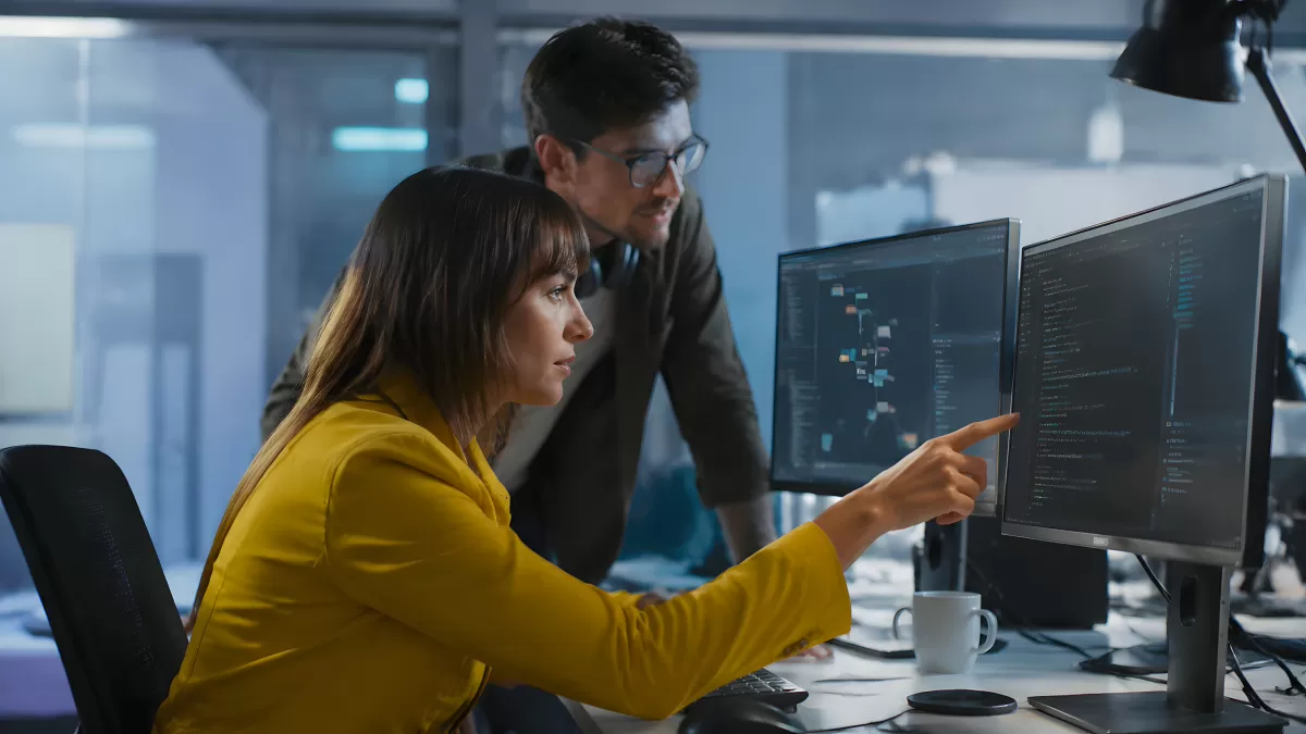 Zwei Entwickler analysieren Code auf Monitoren im Büro