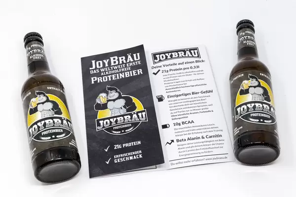 Zwei Flaschen liegend mit Broschüre - Joy Bräu weltweit erstes Alkoholfreies Proteinbier mit hohem Eiweißanteil, BCAA und Carnitin auf weißem Hintergrund