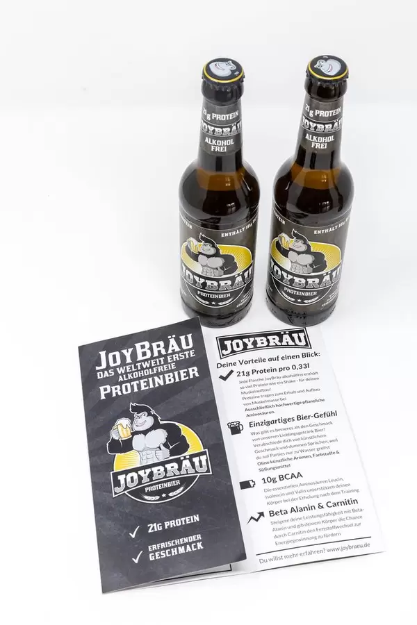 Zwei Flaschen stehend mit Broschüre - Joy Bräu weltweit erstes Alkoholfreies Proteinbier mit hohem Eiweißanteil, BCAA und Carnitin auf weißem Hintergrund