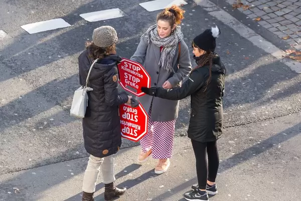 Zwei Frauen bekommen ein Demonstrationsschild mit der Aufschrift: Stop Klimakrise, Stop GroKo